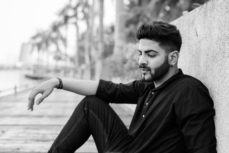 泰国曼谷安静的公园里,年轻英俊的印度男子低头坐在木板路上思考照片