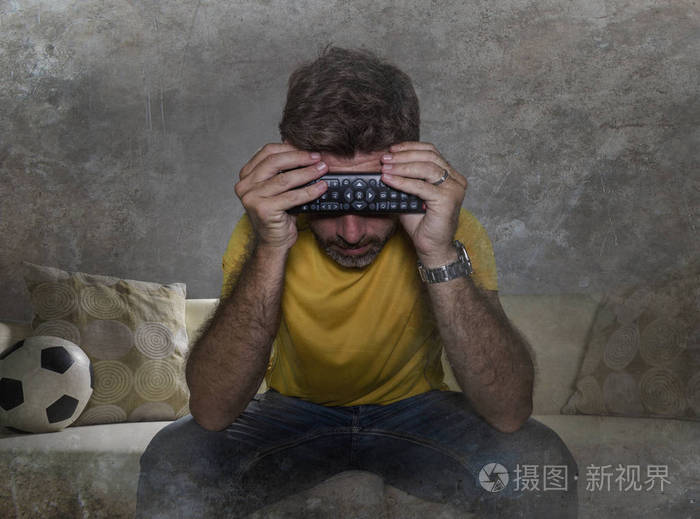 一个沮丧沮丧的男人独自坐在客厅的沙发上看欧洲足球赛对球队的失败
