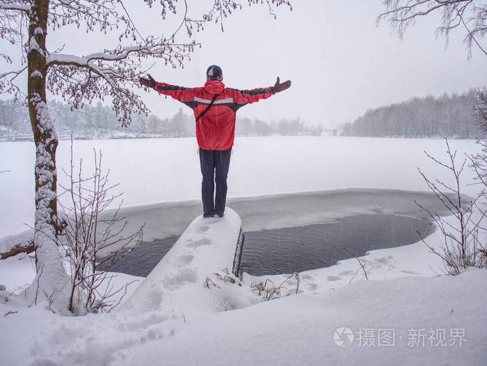 一个穿着红色深色衣服的人站在冬天的雪堤上