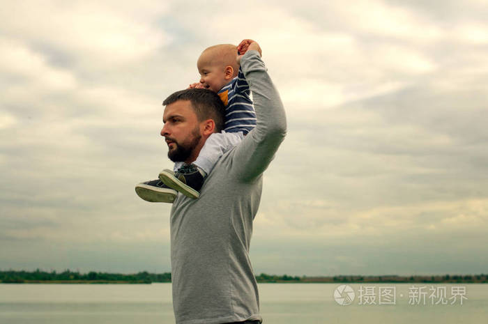 抱在男人怀里的孩子在水边走走孩子和爸爸在天空的衬托下