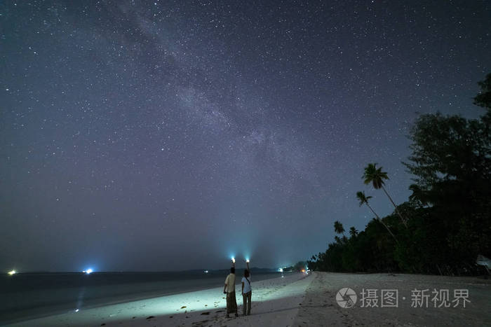 一对夫妇在沙滩上看星星和银河系,夜空中的火炬灯,后视图,真实的人.