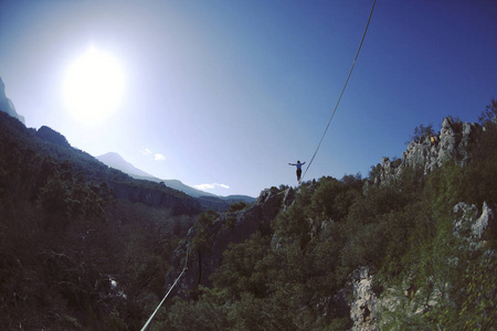 走鋼索一个男人正沿着绷紧的吊索走着.山上的高压线照片