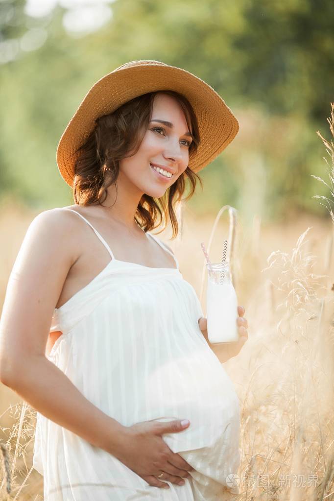 一个年轻的孕妇在美丽的牛奶瓶里喝着牛奶太阳下年轻孕妇的画像夏天