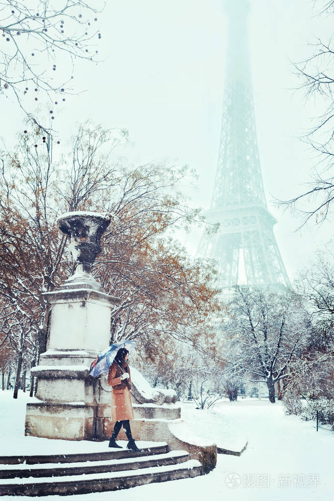 一位身穿米色外套的年轻女子在一个下雪的冬天的巴黎在埃菲尔铁塔的