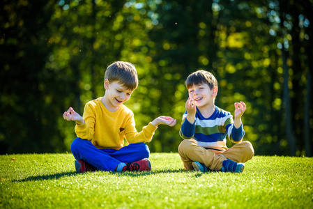 两个白人男孩兄弟朋友穿着便装坐在新鲜的草地上沉思.照片
