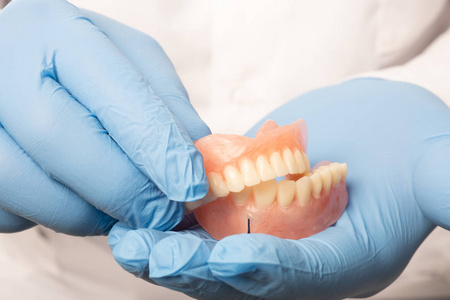 牙齿欢呼一位身穿白大褂的牙医手里拿着一个假牙.健康牙齿的概念.照片