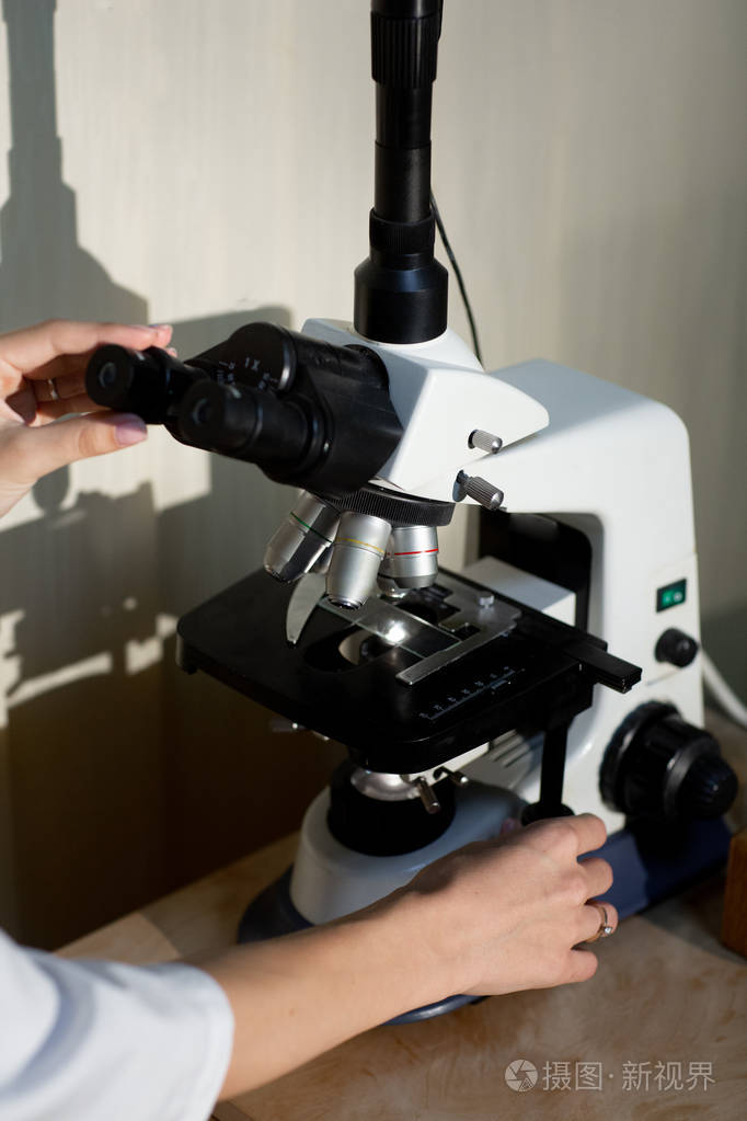 穿着白色医疗制服的女性手的特写镜头在实验室调整显微镜测试健康检查