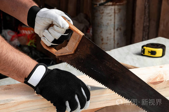 一个木匠用手锯切割木梁男性手用锯子特写用木头干活
