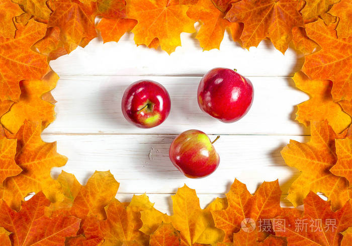 黄色的枫叶和红色多汁的苹果躺在白色的木头背景上