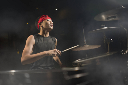 帅气帅气的美籍亚裔青少年,戴着头巾打鼓,表演夜场音乐表演作为业余