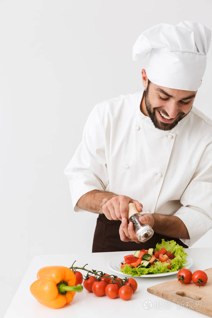 高兴积极快乐的年轻厨师孤立在白色墙壁背景下统一烹饪新鲜蔬菜