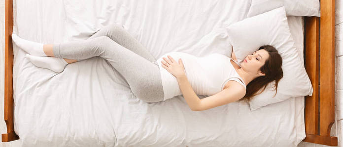 疲惫的孕妇躺在床上,抚摸着肚子照片