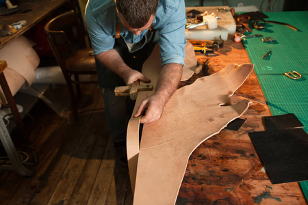 裁缝在车间用皮革缝制围裙,皮带制造过程.照片