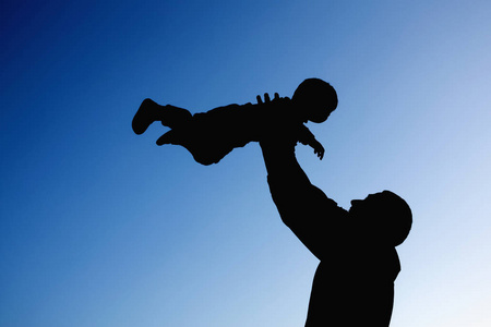 在蓝天背景下玩耍的父子俩的剪影.暑假理念,亲情亲情.照片