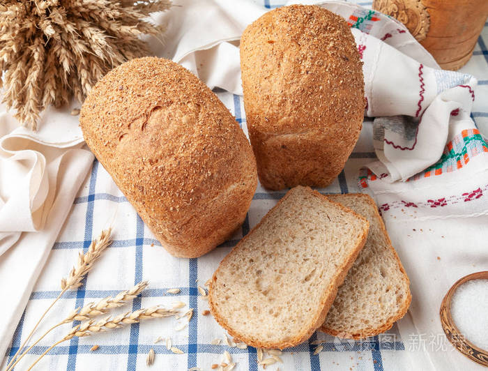 两条麦麸面包.在一块白蓝条纹桌布上.桌布上有两片面包片,麦穗和谷粒.
