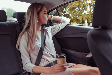漂亮的女商人坐在车内的出租车上,端着杯咖啡茶,吃零食早餐,上班重要