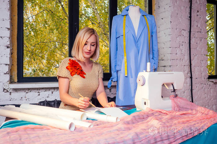 漂亮的金发女裁缝写曲线模板裁缝在车间制作一套服装缝纫机年轻的女