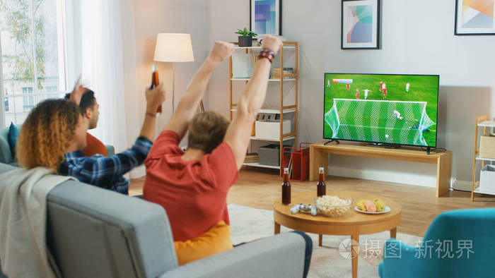 三名体育迷坐在客厅的沙发上观看电视上的重要足球比赛为他们的球队