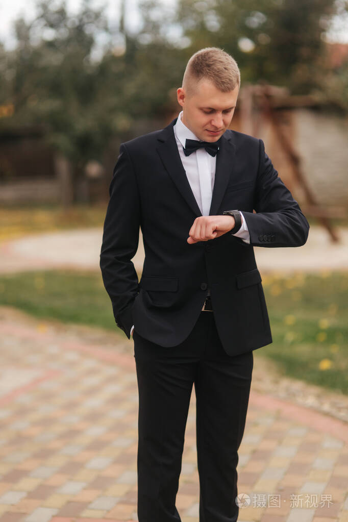 帅气的新郎穿着婚纱在外面秋天黄树的背景黑衣男子系着漂亮的蝴蝶结