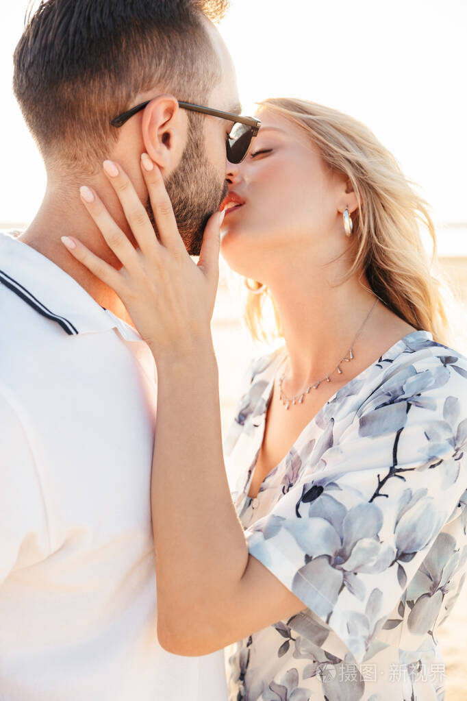 照片中的性感美女情侣穿着夏装在阳光明媚的海滩上亲吻拥抱