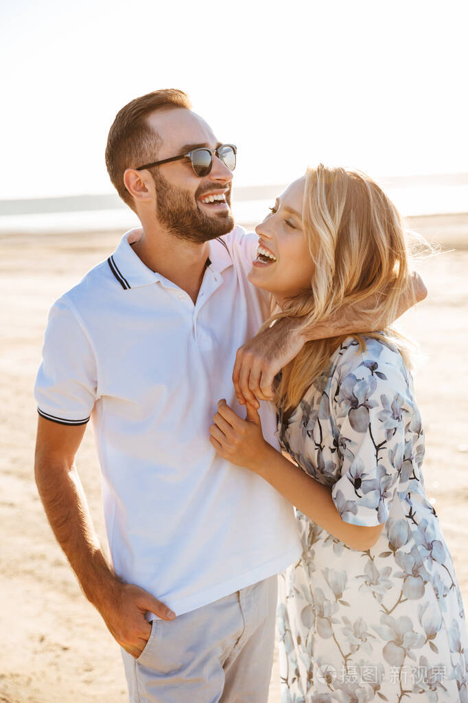 一对幸福的情侣在阳光明媚的沙滩上欢笑拥抱的照片
