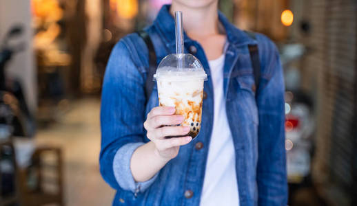 喝红糖在台湾夜市,年轻女子拿着,喝着红糖味的木薯珍珠泡奶茶照片