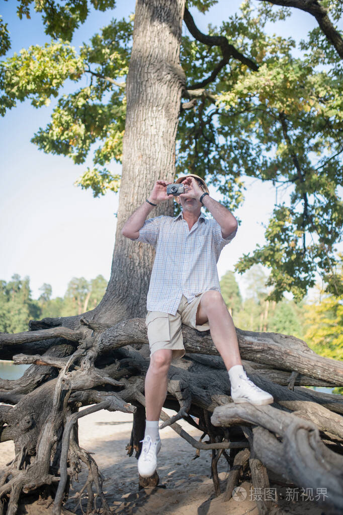 穿短裤的男人坐在树根上拍照