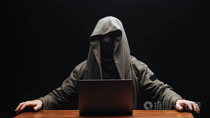 一个没有脸戴着兜帽的黑客黑色的背包上有一台笔记本电脑