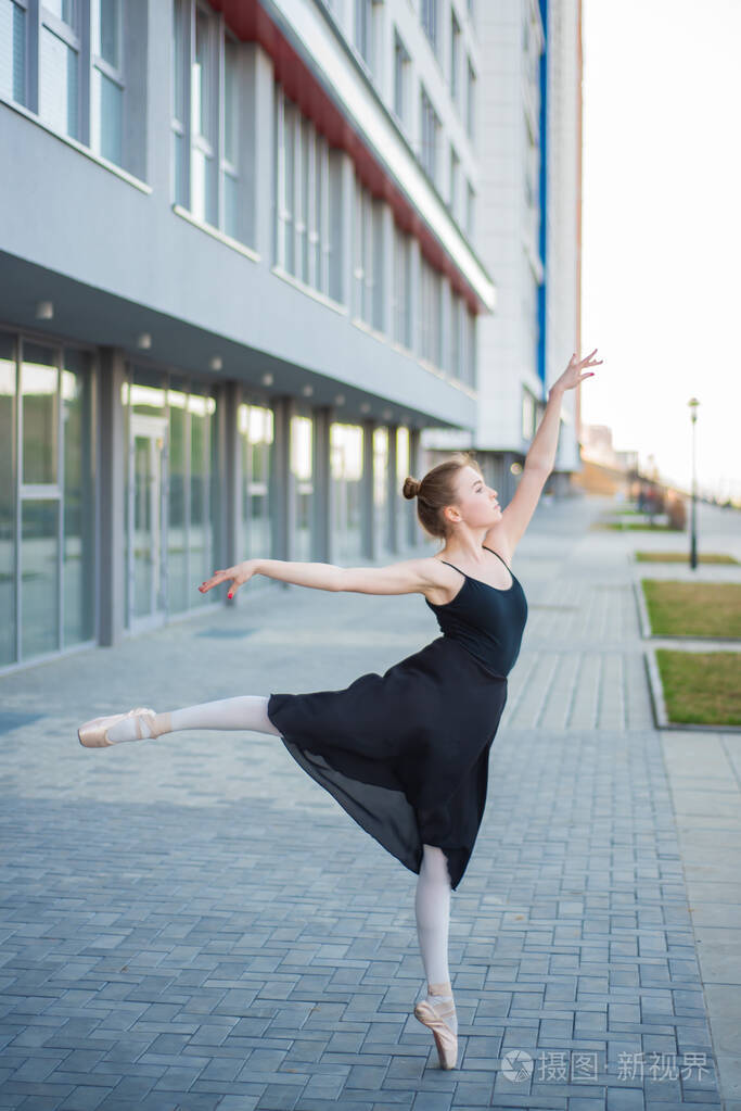 穿着芭蕾舞裙的芭蕾舞演员在住宅楼的背景下摆姿势穿着黑色连衣裙和