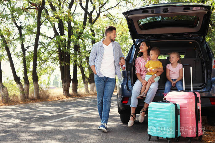 在阳光明媚的日子里一家人在汽车后备箱附近公路旅行