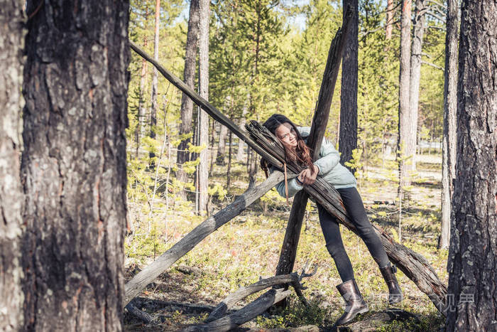 徒步旅行后穿轻便夹克和靴子的女孩被松林中的老树桩吊死