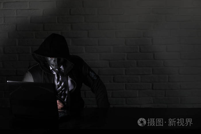 戴着黑色面具和头巾的黑客在桌旁