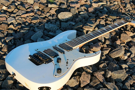 铁轨和石头上的白色电吉他照片