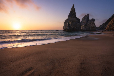 傍晚,在大西洋海岸风景柔和的金色落日余晖中,沙滩上有岩石的剪影照片