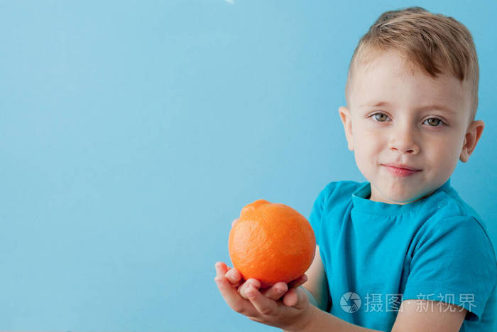 小男孩手里拿着一个橘子，背景是蓝色的