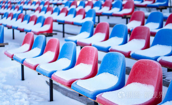 冬季体育场里被雪覆盖的彩色座椅。降雪妨碍运动。不干净的体育场。生态灾害冻结