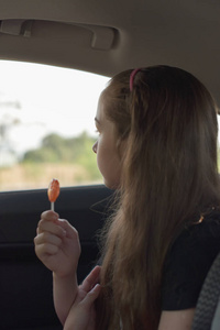 手拿棒棒糖的小女孩坐在车里图片