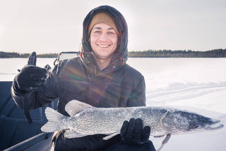 年轻人抱着鱼抓着一条大梭子鱼冰钓照片
