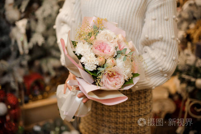 一个女人手里拿着一束娇嫩的粉红色牡丹玫瑰上面点缀着小树枝和绿叶