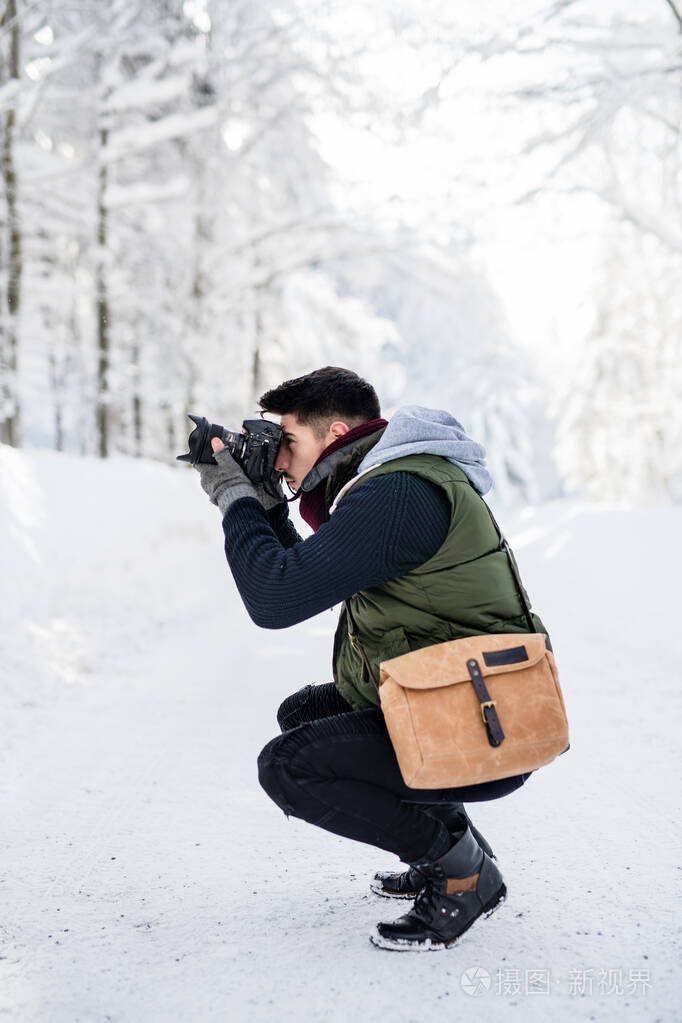 一个年轻人拿着相机站在冬天森林里的雪地里拍照