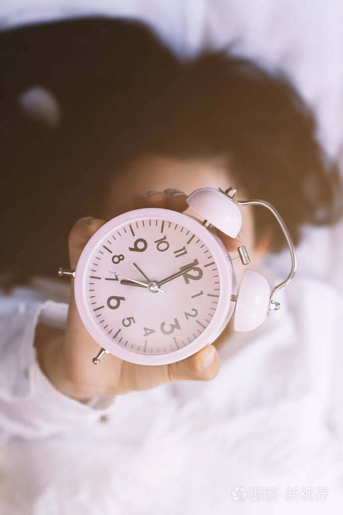 早上好快乐的女人在床上醒来举起闹钟早上7点起床阳光明媚的早晨