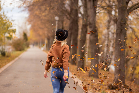 的女孩金发碧眼,穿着棕色保暖毛衣,戴着黑色毡帽,蓝色牛仔裤向前走去