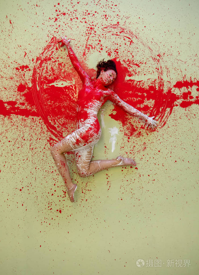 年轻的女人涂上了红色，躺在装饰性的地板上，优雅地跳舞。富有创意富有表现力的人体艺术和绘画。