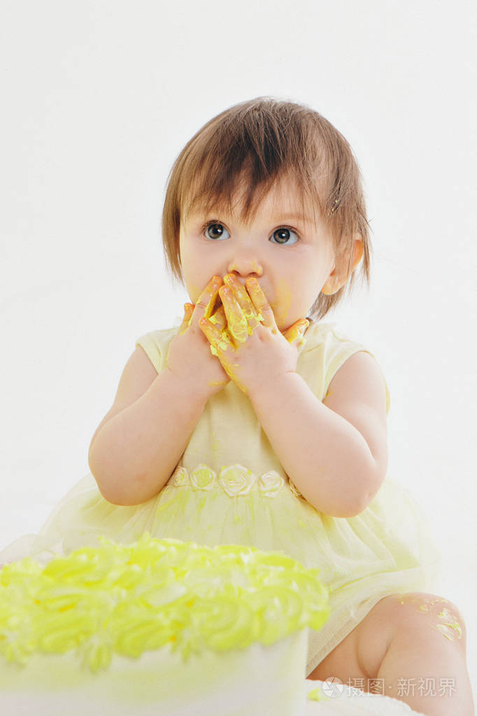 一个小女孩用手在壁炉的壁炉上吃蛋糕婴儿浑身都是食物生日聚会