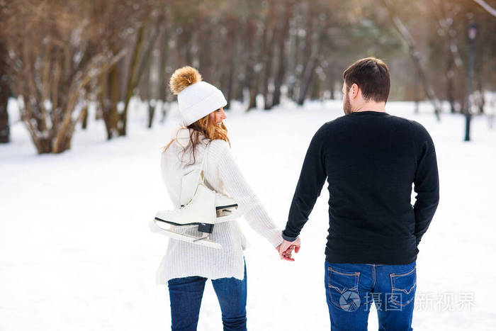 一对情侣在冬季公园散步约会女孩们背上挂着一双溜冰鞋