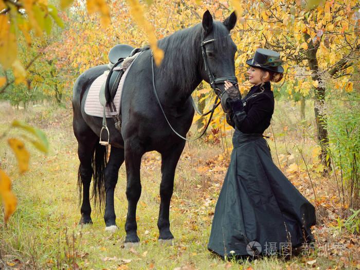穿黑色连衣裙的女骑手牵着一匹黑马