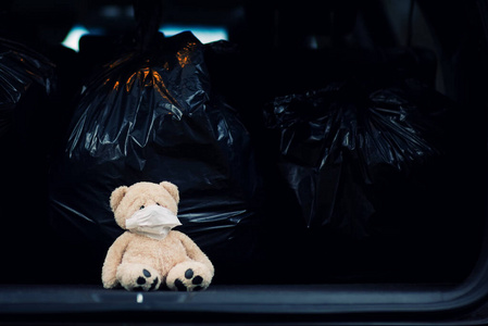 一只戴着医用口罩的泰迪熊和垃圾袋坐在汽车后备箱里照片