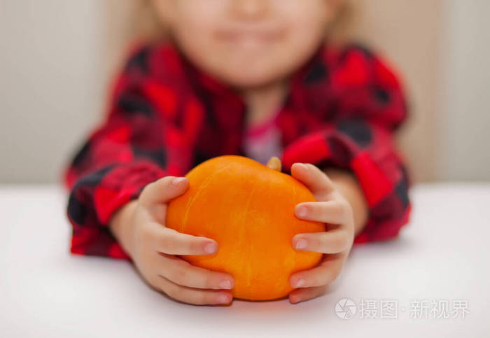 穿格子衬衫的孩子手里拿着一个成熟的南瓜。秋季收获概念