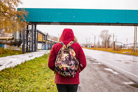 秋天的天气里,一个穿着红夹克背着背包的男人正沿着马路走着照片