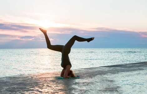 一位身材美丽的女士在海上日出时做瑜伽劈叉,瑜伽姿势的剪影照片